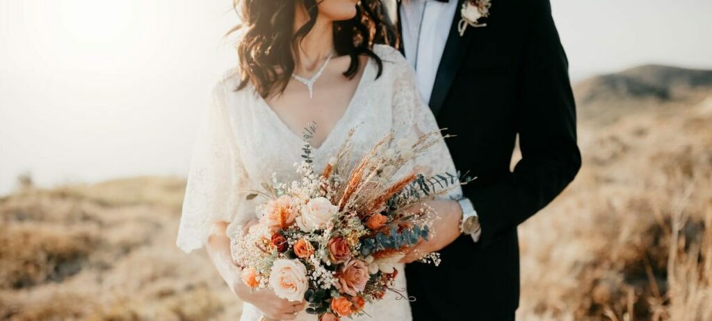 A bride and a groom embracing with a close up of the brides wedding jewelry and rustic wedding bouquet and the grooms watch