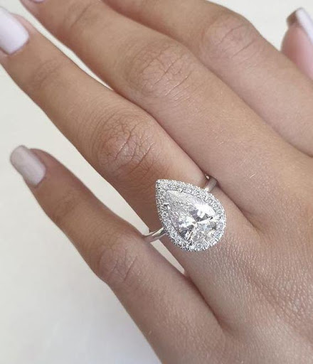 Closeup of a pear shaped engagement ring on a woman's hand with pale pink painted fingernails