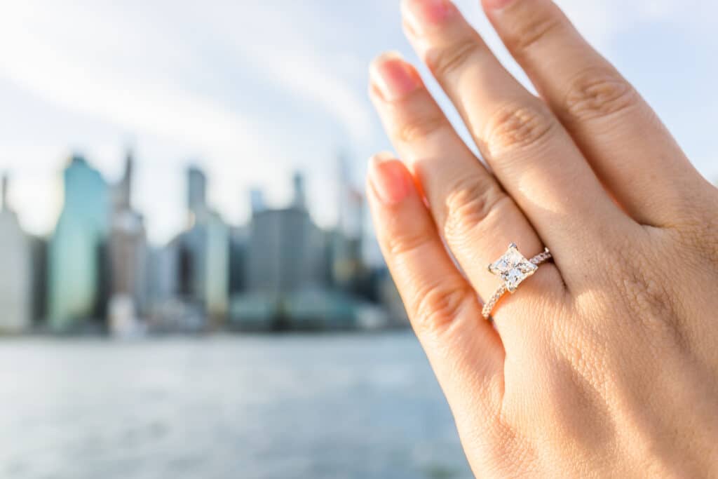 Closeup of a princess cut diamond ring on a hand with a city