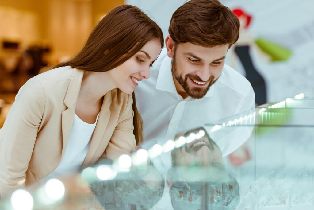 Happy young couple choosing a wedding rings and smiling while looking at different diamond carat weight rings