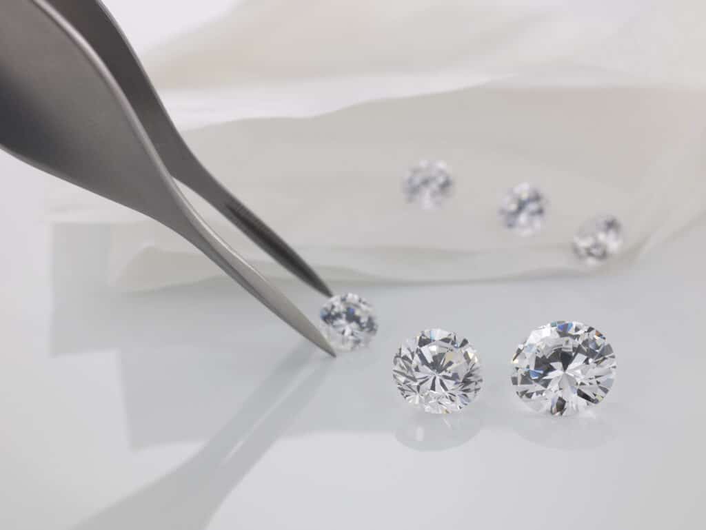 Tweezers and cut diamonds representing diamond carat size