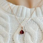 Stylish rose gold necklace with red pendant on cozy cream cable knit sweater.