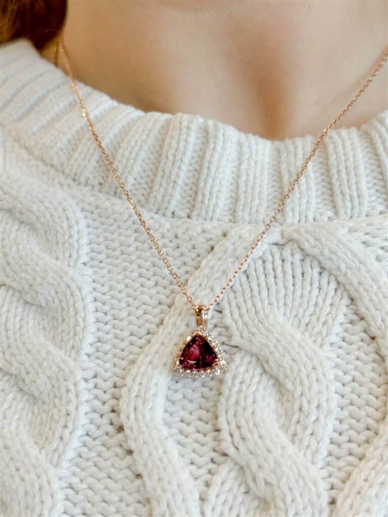 Stylish rose gold necklace with red pendant on cozy cream cable knit sweater.