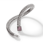 Elegant silver bracelet with pink gemstone clasp, showcasing intricate weaving and stylish design.
