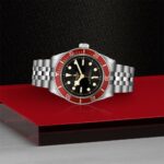 Sleek Tudor wristwatch on glossy red surface, featuring a polished stainless steel case and vibrant bezel.
