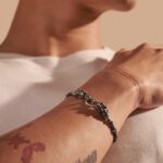 Stylish silver bracelet with colorful beads and tattoos on a tan wrist.