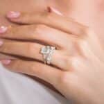 Elegant hand showcasing a diamond engagement ring and stackable bands on a soft pink manicure.