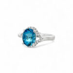 Elegant blue topaz ring with diamond halo in polished white gold, perfect for any occasion.