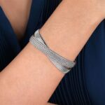 Elegant silver bracelet on a slender wrist against a navy background, showcasing its unique design.