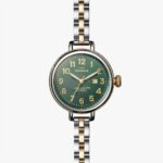 Elegant Shinola watch with gold accents, green face, and a versatile bracelet design.