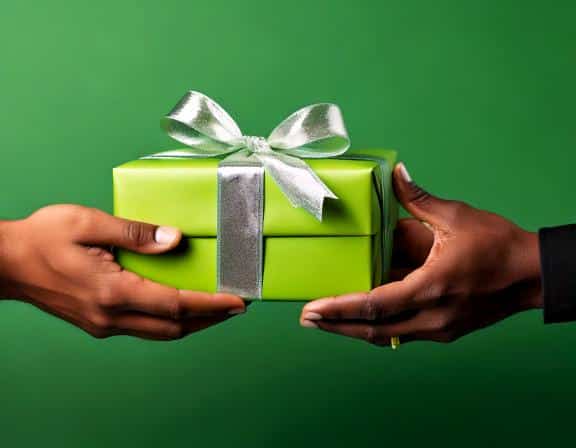 Cheerful hands exchanging a beautifully wrapped green gift box with a silver ribbon.