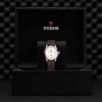Elegant Tudor watch in luxurious black box with leather strap and striking red logo.