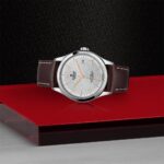Elegant stainless steel watch with rose gold accents and leather strap on textured black background.