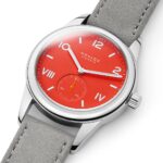 Modern stainless steel watch with vibrant red dial and grey suede strap.