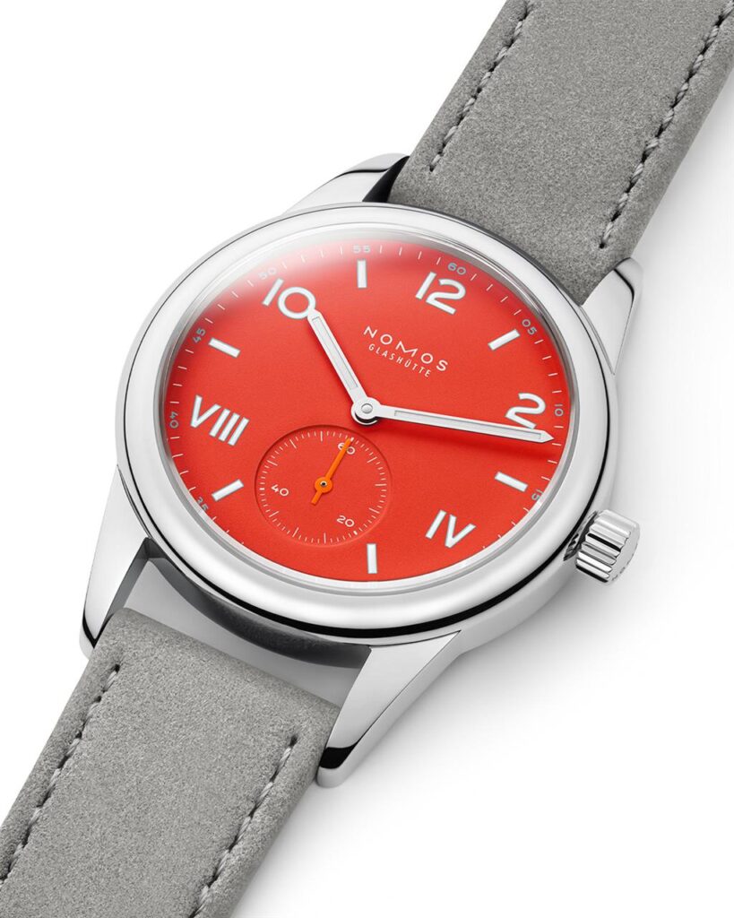 Modern stainless steel watch with vibrant red dial and grey suede strap.