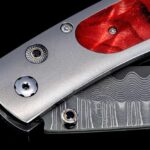Elegant folding knife with a metallic handle and red inlay, showcasing exquisite craftsmanship and design.