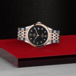Elegant two-tone wristwatch with black dial and rose gold accents on a textured surface.