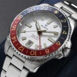 Stylish stainless steel wristwatch with blue-red bezel and white dial on navy cushion.