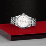 Elegant Tudor watch with stainless steel case, white dial, and vibrant orange accents.
