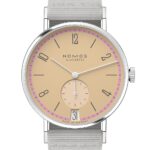 NOMOS Glashütte minimalist watch with beige dial and pink accents on gray fabric strap.
