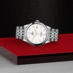 Elegant Tudor watch with silver casing and rose gold accents on a glossy red background.