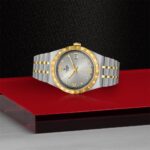 Luxurious Tudor watch with gold bezel and stainless steel bracelet on a refined red surface.
