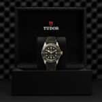 Elegant Tudor watch in black presentation box, featuring gilded accents and a textured green strap.