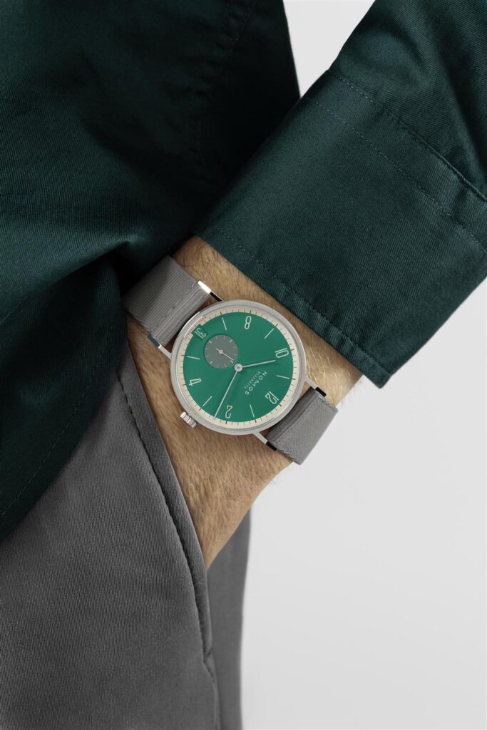 Stylish wristwatch with green dial and gray strap on a persons wrist in a green shirt.