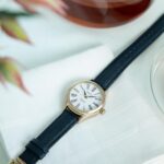 Elegant gold-tone watch on a white napkin, featuring a navy blue leather strap and Roman numerals.