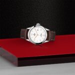 Elegant Tudor watch on red platform with stainless steel case and brown leather strap.