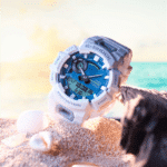 G-SHOCK watch in blue and white on sandy beach, evoking outdoor adventure and relaxation.