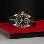 Elegant Tudor watch with black dial, gold accents, and leather strap on a reflective surface.