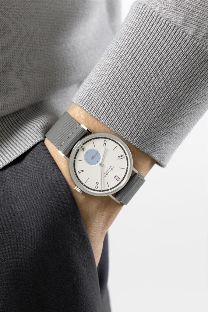 Elegant wristwatch with white dial and blue sub-dial, showcased against a stylish gray sweater.