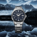 Seiko automatic watch in stainless steel with blue dial, set against a scenic mountain backdrop.