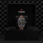 Elegant Tudor watch in luxury box, featuring a black dial and gold accents on brown leather strap.