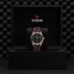 Luxury black dial Tudor watch in elegant packaging with brown leather strap and date function.