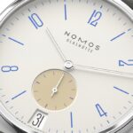 Elegant NOMOS Glashütte wristwatch with minimalist design, ivory dial, blue indices, and polished stainless steel case.