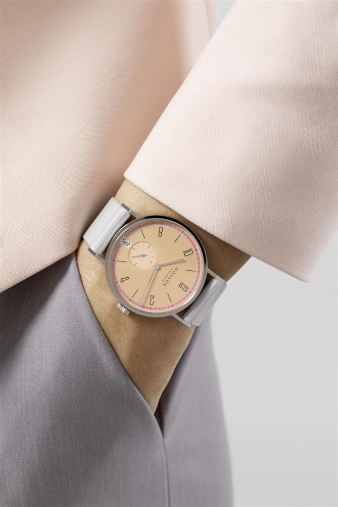 Stylish silver watch with peach dial worn with chic blouse, perfect for casual or formal wear.