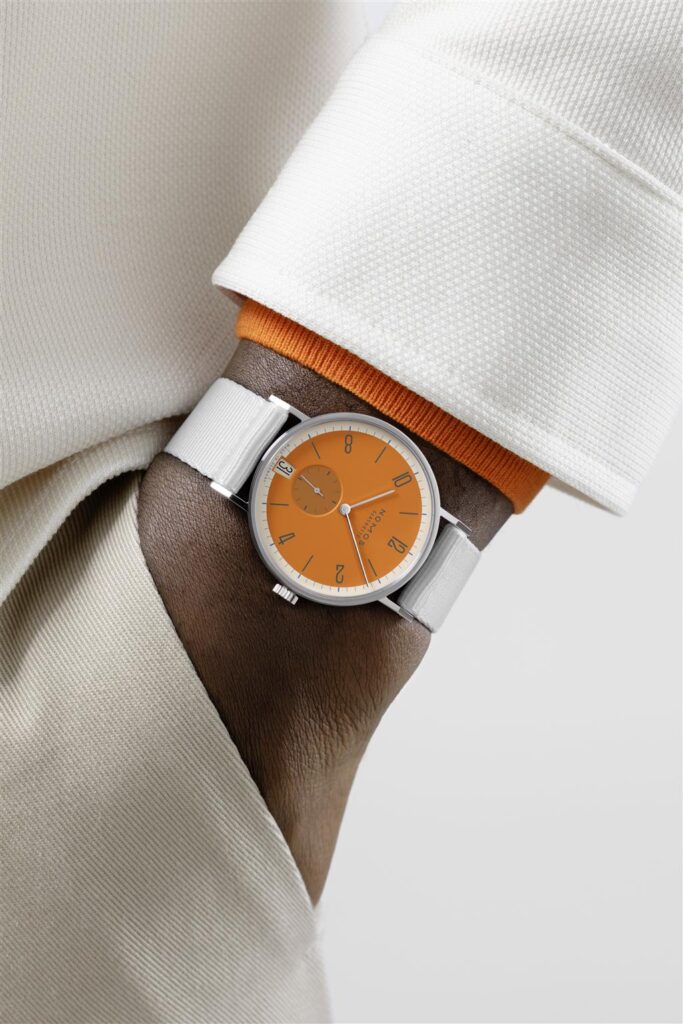Stylish orange dial watch on a wrist with elegant sleeve and coordinated accessories.