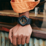 Stylish wristwatch on a hand in an orange shirt against a rustic wooden background.