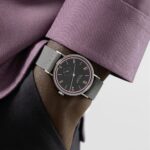 Stylish wristwatch on dark skin, featuring vibrant pink accents and an elegant lavender shirt sleeve.