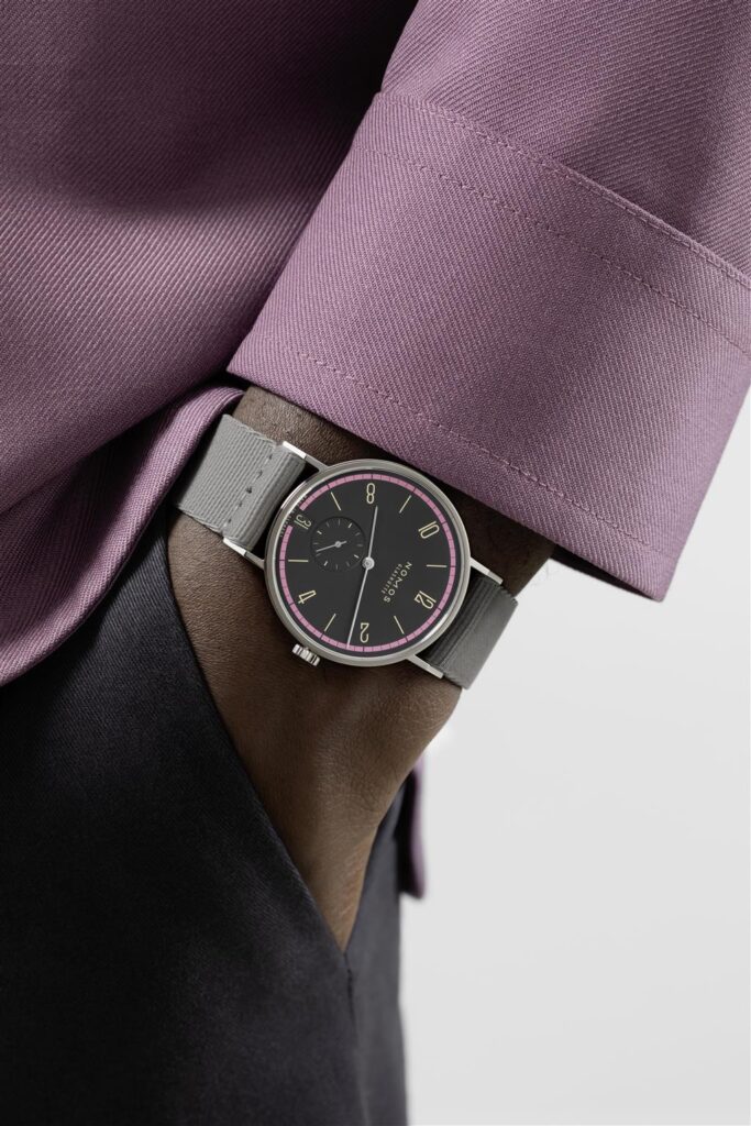 Stylish wristwatch on dark skin, featuring vibrant pink accents and an elegant lavender shirt sleeve.