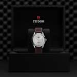 Luxurious Tudor watch in stylish black box, featuring a silver face and brown leather strap.