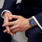 Well-groomed gentleman in a navy suit showcasing an elegant watch with a blue dial.