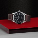 Tudor luxury watch with stainless steel case and brown leather strap on vibrant red display.