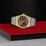 Tudor luxury watch with gold accents and diamond markers on a reflective red surface.