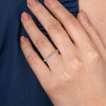 Elegant hand wearing a delicate silver ring with sparkling gemstones against a soft blue background.