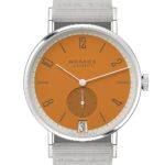 NOMOS Glashütte watch features an orange dial, stainless steel case, and grey fabric strap.