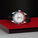 Tudor watch with stainless steel case, blue and red bezel, and black fabric strap.