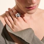 Elegant silver ring on manicured hand, adorned with a cozy olive green sweater.